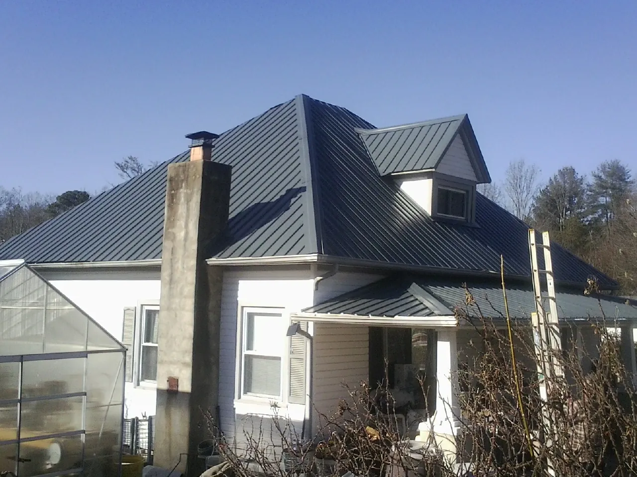 Dark blue standing seam metal roof on a white farmhouse with dormer — Slate & Tile Roof Repair by Roofing Brothers in Clyde