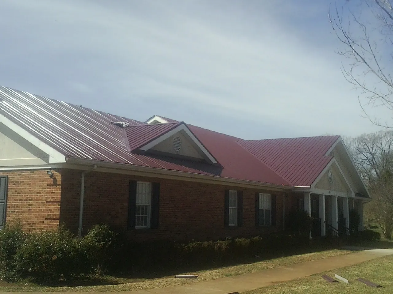 Red metal roof with gabled entries on a long brick building, from a Hail Damage Roof Repair job in Clyde