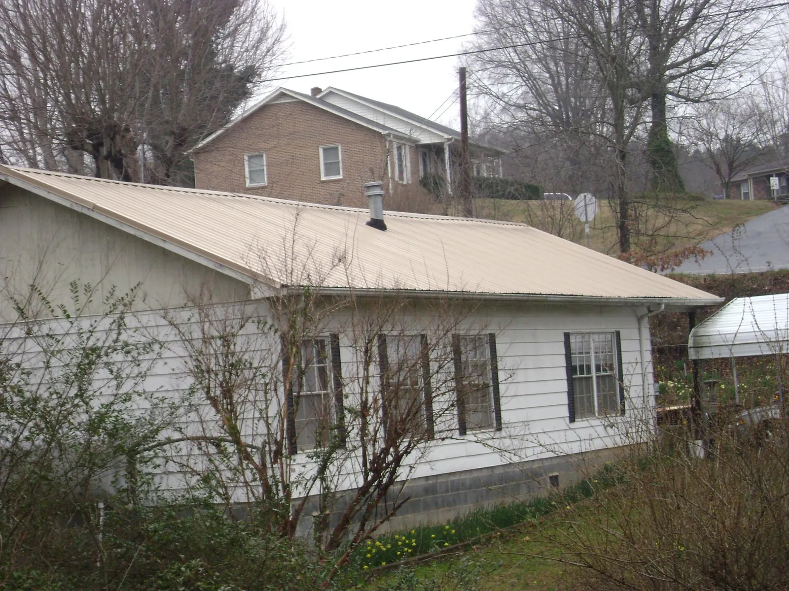 Tan metal roof on a white sided house set into a hillside — Commercial Roofing by Roofing Brothers in Clyde