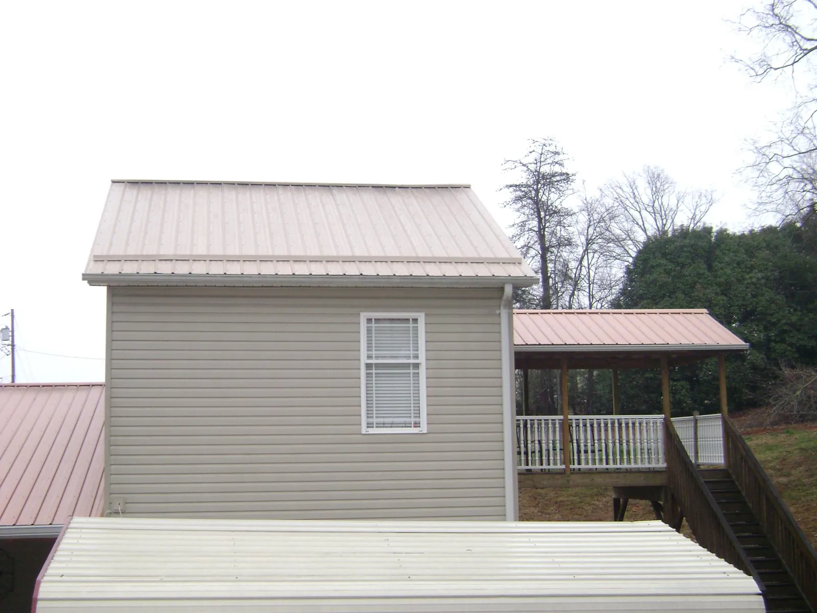 Tan metal roofs on a two story addition and attached porch, from a Roof Replacement job in Clyde